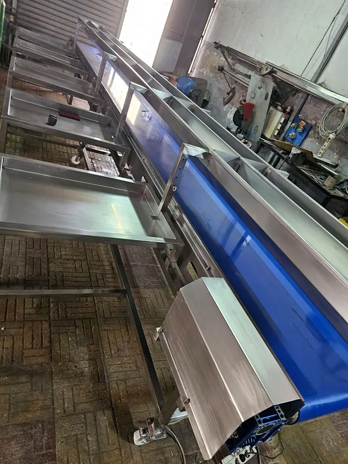Convoyeur inox avec bande bleue à côté d'une table de travail en inox